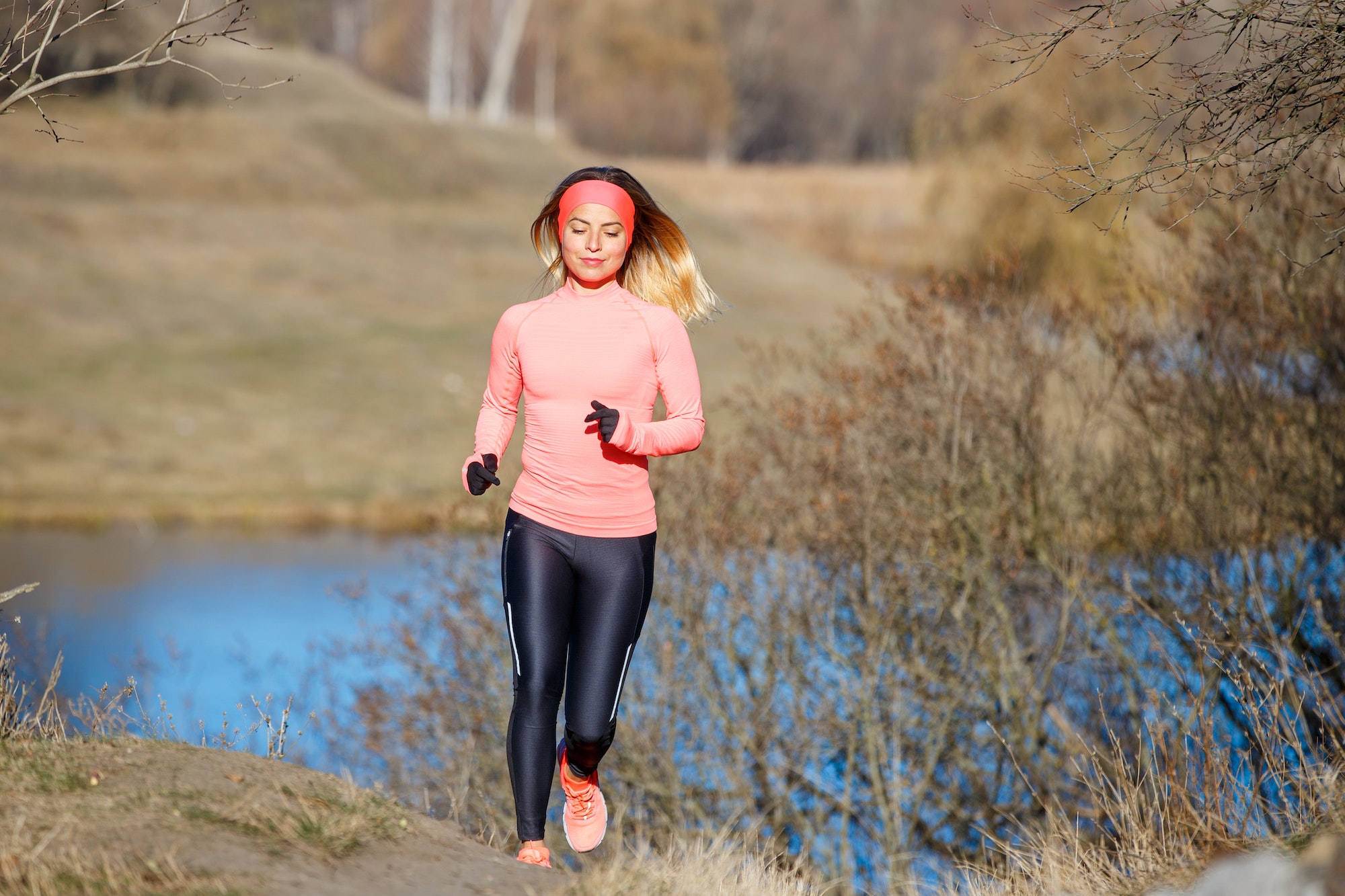 Young woman jogging in the park near the pond in the cold sunny morning